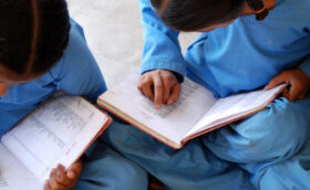 Two little girls are studying something with their school attire, keeping their notes on the lap.