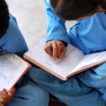 Two little girls are studying something with their school attire, keeping their notes on the lap.